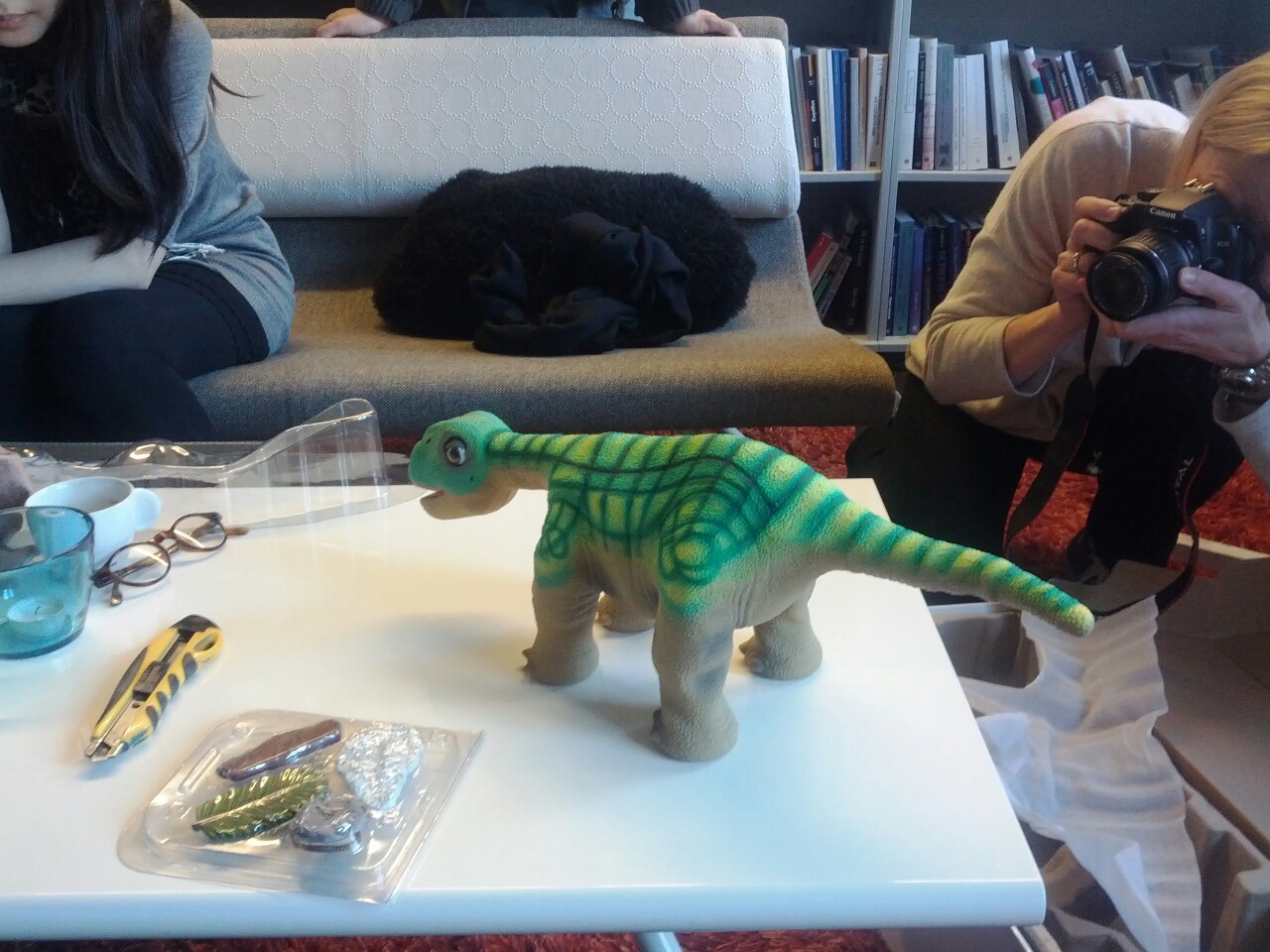 Pleo robot dinosaur on a table while a person photographs it